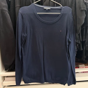 Mörkblå långärmad tröja från Tommy Hilfiger - Säljer en klassisk mörkblå långärmad tröja från Tommy Hilfiger med rund halsringning. Tröjan har en liten broderad logga på bröstet och är tillverkad i ett tunt, mjukt material. 