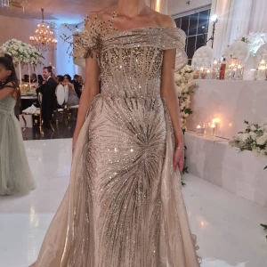 Glittrig guldig, bronsig långklänning med offshoulder - Säljer en fantastisk guldig långklänning med glittriga paljetter och offshoulder-modell. Klänningen har en vacker omlott-detalj upptill och ett elegant släp. Perfekt för bal eller fest där du vill glänsa extra mycket. PRIS KAN DISKUTERAS💕