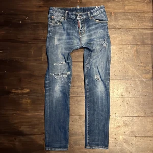 Blå slim jeans från Dsquared2 - Säljer ett par blå jeans från Dsquared2 med slitna detaljer och lätt tvättad look. Klassisk femficksmodell med knappgylf och Dsquared2-logga på läderpatch bak samt röd etikett fram. Nypris 4000kr+, självklart äkta. Tveka inte att höra av dig vid fundering👍😁