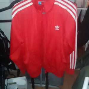 Adidas (tjej) Röd dragkedjs tröja.  - Storlek M använd endast 2 gånger. Klarröd färg med vita detaljer stort Adidas märke på ryggen.  Pris 300kr då ingår frakt kostnad om den ska skickas. 