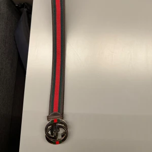  bälte  - Bältet har ränder i grönt och rött längs hela bandet och detaljer i brunt skinn. Perfekt accessoar för att lyfta din outfit. Tror den är runt 85 cm lång 