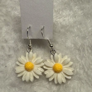 Örhängen med prästkrageblommor - Säljer ett par söta örhängen med prästkrageblommor i vitt och gult. Blommorna är detaljerade och hänger i silverfärgade krokar. Perfekt för dig som vill ha en lekfull och somrig accessoar! Krokarna är i sterling silver 