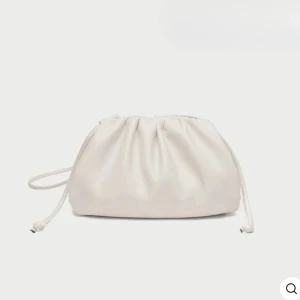 Vit clutch väska - Säljer en stilren vit axelväska med mjuk form. Perfekt för dig som gillar minimalistisk design och vill ha en enkel men snygg accessoar till din outfit. Passar både till festliga tillfällen som bal och utgång men även till vardags för lite extra lyx. Bredd: 26cm Djup: 10cm Höjd: 16cm. helt ny aldrig använd obruten i det som sitter ihop det längre bandet.