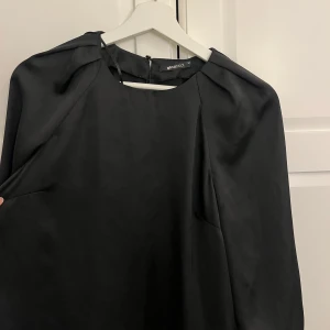 Svart satintopp från Gina Tricot - Säljer en elegant svart satintopp från Gina Tricot med rund halsringning och trekvartsärm. Toppen har en lätt glansig finish och en enkel, stilren design som passar perfekt till många olika tillfällen.