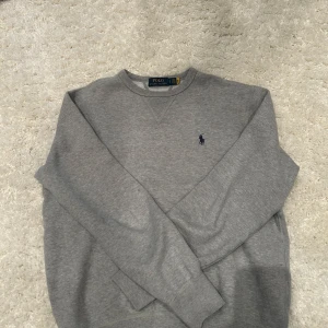 Grå sweatshirt från Polo Ralph Lauren - Säljer en stilren grå sweatshirt från Polo Ralph Lauren med det klassiska broderade logotypen på bröstet. Tröjan har en rund halsringning och långa ärmar, perfekt för en avslappnad look. Skick 9/10. Självklart äkta | nypris ~2200kr