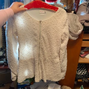 Vit kofta med struktur från Chloé London - Säljer en vit kofta från Chloé London med dekorativt strukturmönster och dragkedja framtill. Koftan har lång ärm och rund halsringning, perfekt för att lyfta en enkel outfit.