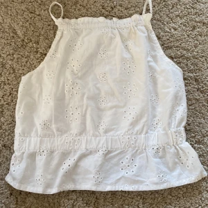 Vit broderad linnetopp från H&M - Säljer en söt vit linnetopp från H&M med broderade blommor och tunna axelband. Toppen har en luftig passform och fina hålbroderier som ger en somrig känsla.