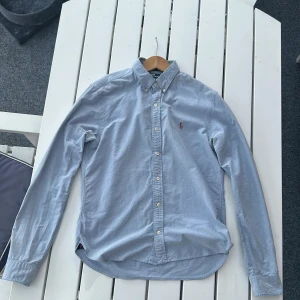 Ljusblå skjorta från Polo Ralph Lauren - Säljer en ljusblå skjorta från Polo Ralph Lauren i slim fit-modell. Skjortan har klassisk krage, knäppning framtill och broderad logga på bröstet. Perfekt för dig som gillar stilrena och tidlösa plagg.
