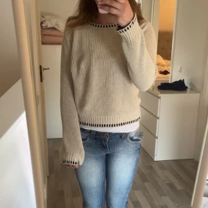 Beige stickad tröja med svarta detaljer från Free/Quent - Säljer en beige stickad tröja från Free/Quent i storlek S. Tröjan har svarta ränder vid halsringning, ärmslut och nederkant. Den är långärmad och har en avslappnad passform. Perfekt för lager-på-lager-stil.