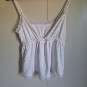 Vit linnetopp med spetsdetaljer - Söt vit linnetopp med tunna axelband och spetsdetaljer längs halsringning och nederkant. Perfekt för varma dagar eller som ett lager under en kofta. Mjuk och luftig känsla 🩷 inga defekter och sparsamt använd! Skriv vid frågor!