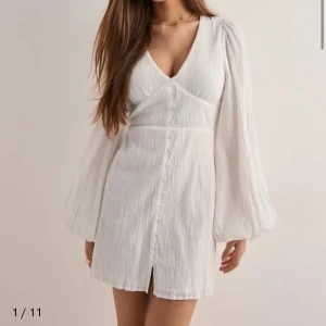 Vit kortklänning med v-ringning och knappar - Vit strukturerad klänning från Nelly. har endast testat den på så i nyskick! Perfekt till sommaren/student!😊