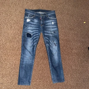 Blå slitna jeans från Dsquared2 - Säljer ett par blå jeans från Dsquared2 med slitningar och hål på benen. Jeansen har en slim passform och klassisk femficksdesign. Snygga detaljer med slitna partier och lite färgstänk för en cool look.