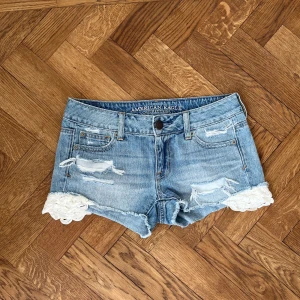 Ljusblå jeansshorts med spets från American Eagle - Säljer ett par ljusblå jeansshorts från American Eagle med slitna detaljer och vit spets längst ner på benen. Ungefär 36/34 i storleken 