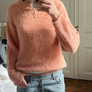 Persikofärgad stickad tröja - Mysig persikofärgad stickad tröja med lång ärm och rund hals. Tröjan har en lätt oversized passform och är perfekt för lager-på-lager. Mjuk och fluffig känsla, passar till både jeans och kjol.