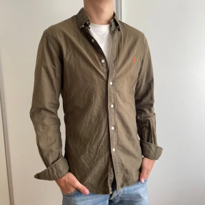 Olivgrön skjorta från Polo Ralph Lauren - Säljer en olivgrön skjorta från Polo Ralph Lauren med klassisk krage och knappar framtill. Tröjan är i mycket bra skick och storlek S. Tveka inte på att skriva om du har frågor! 🤩
