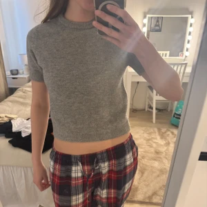 Grå croppad stickad tröja - Säljer en enkel och stilren grå croppad stickad tröja med korta ärmar och rund hals. Perfekt att matcha med både jeans och kjol för en avslappnad look.