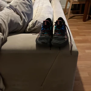 Nike Kyrie basket skor med färgglada detaljer - Säljer ett par Nike Kyrie basket skor i svart med färgglada detaljer i blått, rött och orange. Skorna har snörning och en platt sula, perfekt för dig som gillar basket och vill sticka ut på planen.