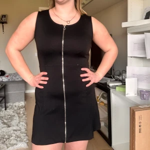 Svart ärmlös klänning med dragkedja - Säljer en svart, ärmlös kortklänning med markerad midja och dragkedja framtill. Säljer den då tyvärr för att den har blivit för liten. Men klänningen har en enkel och stilren design som passar perfekt till många tillfällen. Materialet känns mjukt och stretchigt. 