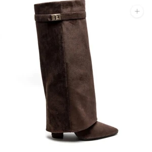 Bruna höga stövlar i mocka - Säljer ett par bruna höga stövlar i mjuk mocka med dekorativt bälte upptill. Skorna har spetsig tå och en stilren design som passar perfekt till klänning eller kjol nu i sommar. Skorna är använda en gång och är i fint skick. 