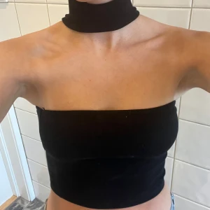 Svart tubtopp med choker - Säljer en svart tubtopp med chocker . Toppen är axelbandslös och har en tight passform. Toppen är i storlek XS men passar Xs-M