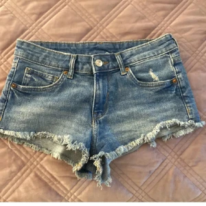 Blå jeansshorts med fransar - Snygga blå jeansshorts med fransiga kanter och klassisk femficksdesign. Perfekta för varma dagar och har en avslappnad vibe. Stängs med knapp och dragkedja framtill.