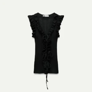 Svart volangtopp med knyt från zara - Säljer en svart topp med volangdetaljer längs ärmhålen och v-ringning. Toppen har knyt framtill och är ärmlös, vilket ger en trendig och feminin look. Perfekt att styla till både jeans och kjol.
