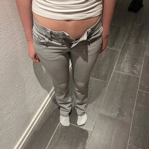 Ljusgrå bootcut jeans - Säljer ett par ljusgrå jeans med bootcut passform och låg midja. Jeansen har klassiska fem fickor, dragkedja och knapp framtill. Perfekta för en avslappnad och trendig look. OBS fläckar på framsidan, syns på bild 4. Hör av er gällande andra frågor eller fler bilder.💛