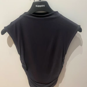 Svart ärmlös klänning från Gina Tricot  - Säljer en svart ärmlös klänning från Gina Tricot med rund halsringning och draperad detalj i sidorna. Klänningen har en enkel och stilren design som passar perfekt till många tillfällen.