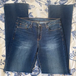 Blå bootcut jeans från Calvin Klein Jeans - Snygga blå jeans från Calvin Klein Jeans med bootcut-modell och klassiska orange sömmar. Byxorna har fem fickor och stängs med knapp och dragkedja. Perfekta för dig som gillar en tidlös jeansstil.