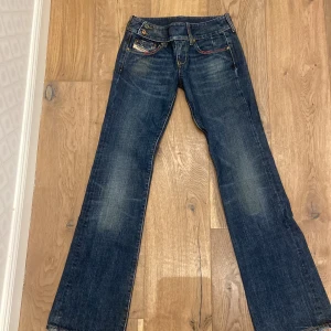 Mörkblå diesel jeans - Coola mörkblå diesel jeans med orange broderier på bakfickorna i bra skick. Raka/bootcut ben och ett ”bälte” därfram som sitter fast 💗 Vet tyvärr inte storleken då det inte har funnits någon lapp.                                      Grenhöjd: 19 cm Innerbenlängd: 77 cm Midjemått raktöver: 37 cm, skriv gärna för mer mått eller bilder! 🥰