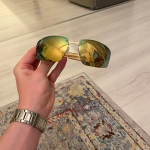 Guldiga sportiga solglasögon från Eytys - Säljer ett par spegelglasade solglasögon från Eytys med guldfärgade bågar och stora, rundade linser i gult och grönt. Kommer med originalfodral och påse. Perfekta för dig som vill sticka ut med en sportig look.