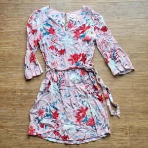 Sommarklänning från Vintage Stories liten 42 - Söt blommig knälång klänning från Vintage Stories i ljusrosa med röda, vita och blå blommor. Klänningen har trekvartsärm, knytband i midjan och v-halsringning. Perfekt för sommarens alla tillfällen! Liten 42, uppskattar den mer som 40! Använd 2 ggr så toppenskick. Fler bilder finns. Svalt skönt tyg, ofodrad.