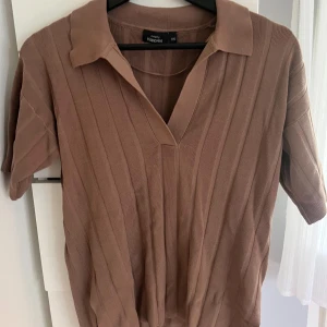 Brun ribbad tröja  - Säljer en brun ribbad tröja från Kappahl i storlek XS. Tröjan har korta ärmar, snygg krage och v-ringning. Stilren och inga tecken på användning, max använd 2 gånger. Snygg att matcha med jeans eller kjol!