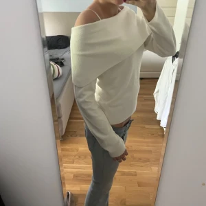 Vit offshoulder stickad tröja - Säljer en snygg vit stickad tröja med offshoulder-design. Tröjan har lång ärm och bred ribbad kant upptill som ger en modern look. Perfekt att styla med jeans eller kjol. Aldrig använd ❣️ 
