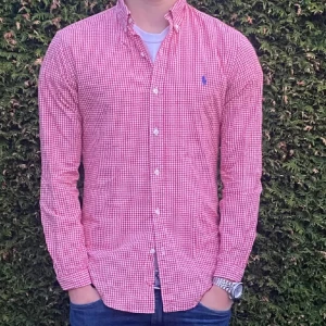 Rosa och vitrutigt skjorta från Ralph Lauren - Säljer en klassisk rosa- och vitrutigt skjorta från Ralph Lauren med button-down krage och blå broderad logga på bröstet. Skjortan har långa ärmar och vita knappar framtill. Perfekt till jeans eller chinos! Finns s och m