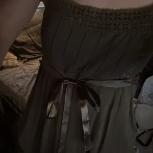 Brun klänning med spets och rosett från H&M - Supersöt brun klänning från H&M med spetsdetaljer upptill och ett satinband i midjan som knyts till rosett. 