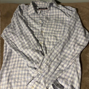 Vit och blå rutig skjorta från Oscar Jacobson - Klassisk vit skjorta med blått rutmönster från Oscar Jacobson. Skjortan har lång ärm och knäppning framtill med vita knappar. Perfekt för en stilren och tidlös look.