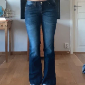 Blå bootcut jeans - Säljer ett par klassiska blå bootcut jeans med normal passform och låg midja. Jeansen har fem fickor, dragkedja och knapp framtill samt snygga slitningar på benen. Perfekta för dig som gillar en tidlös denimlook.de är uppsprättade längst ner