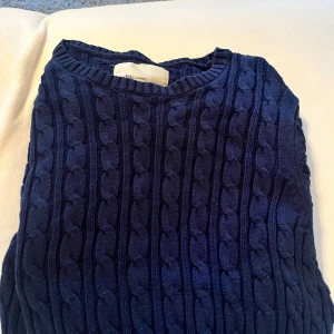 Mörkblå kabelstickad tröja från Iconic Sport - Säljer en mörkblå kabelstickad tröja från Iconic Sport i storlek medium. Tröjan har klassiskt flätmönster och rund halsringning, perfekt för kyligare dagar.
