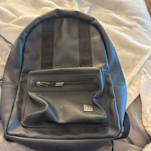 Svart ryggsäck från Db - Säljer en DB ryggsäck. Modellen heter ÆRA 16L BACKPACK. Har små fläckar som syns på bilderna, annars som ny
