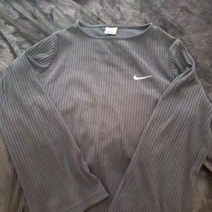 Svart ribbad långärmad tröja från Nike - Säljer en svart långärmad tröja från Nike med diskret ribbad struktur och klassisk Nike-logga på bröstet. Perfekt för en avslappnad och sportig stil. Materialet är mjukt och stretchigt för extra komfort. Helt fläckfri 