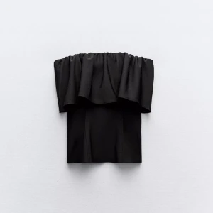 Svart axelbandslös volangtopp - Snygg svart axelbandslös topp med volangdetalj upptill. Perfekt för en trendig och stilren look. Toppen har en rak passform och är enkel att matcha med både byxor och kjol.