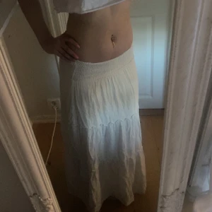 Vit långkjol med volang - Säljer en vit långkjol med bred resår i midjan och volangdetaljer. Kjolen är luftig och har en avslappnad passform, perfekt för varma dagar.