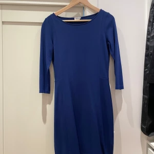 Blå klänning från Filippa K - En stilren blå klänning från Filippa K med trekvartsärm och rund halsringning. Klänningen har en figurnära passform och är tillverkad i en mjuk blandning av viskos, polyester och elastan. Perfekt för dig som gillar enkel och klassisk stil.