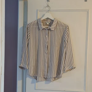Unik o fin randig skjorta från Monki med snygg rygg! - Säljer en vit skjorta med svarta vertikala ränder från Monki. Skjortan har klassisk krage, knäppning framtill och trekvartsärmar med knapp. Passformen är lite loose och materialet känns lätt och luftigt. Fina veck i ryggen!