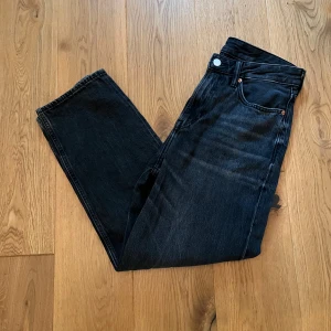 Svarta loose fit jeans från H&M - Säljer ett par svarta jeans från H&M med loose fit. Klassisk femficksmodell med raka ben och normal midja. Jeansen är tillverkade i denim och har knapp- och dragkedjegylf.