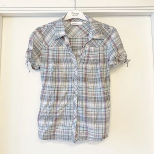 Skjorta  - Söt rutig skjorta i figursydd modell med lite puffärmar med knyt i jättefint skick. Kommer i ett tunt bomullstyg utan stretch. Säljer den billigt för att den saknar 1 knapp, men finns ny att sy fast