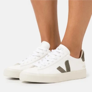 Vita sneakers från Veja med grå detaljer - Snygga vita sneakers från Veja med kaki grön V-logga på sidan och hälflik. Skorna har klassisk snörning och platt sula, perfekt för en stilren vardagslook. Tillverkade i skinn och syntetmaterial. nästan aldrig använda, som nya