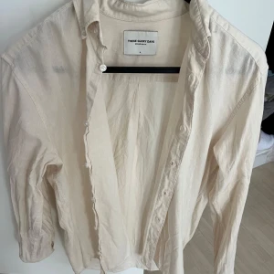 Beige skjorta från These Glory Days - Säljer en stilren beige skjorta från These Glory Days. Skjortan har klassisk krage, långa ärmar och knäppning framtill. Materialet känns mjukt och lätt mot huden.