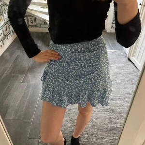 Blå blommig kjol - Säljer denna supersöta kjolen😍 Kjolen har omlottdesign med knyte i sidan som passar perfekt till sommaren💗